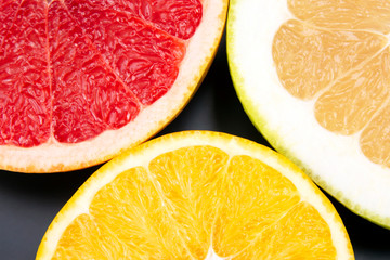 cut pieces of different citrus fruits on dark background