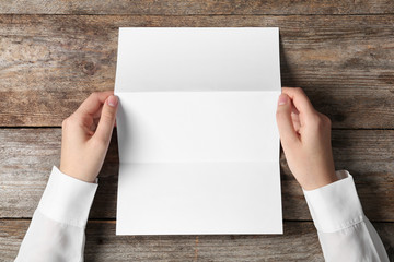 Woman holding blank brochure mock up on wooden table, top view