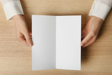 Obraz premium Woman holding blank brochure mock up on wooden table, top view