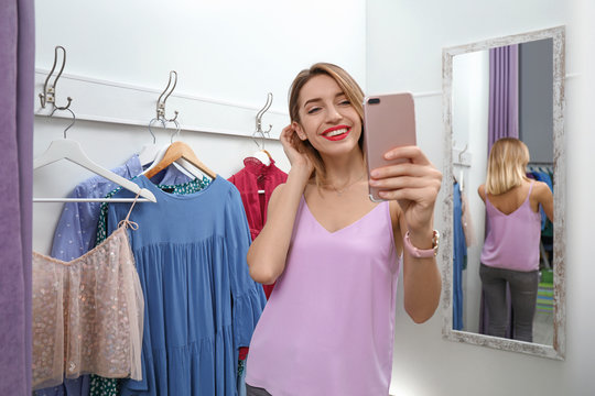 Young woman taking selfie in dressing room. Fashion store