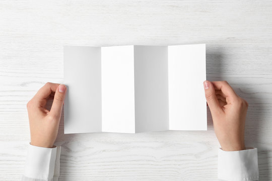 Woman holding blank brochure mock up on light background, top view