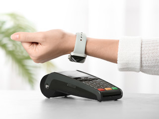 Woman using terminal for contactless payment with smart watch at table, closeup