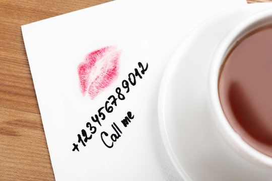 Paper Napkin With Phone Number And Lipstick Mark Under Tea Cup On Wooden Table, Top View