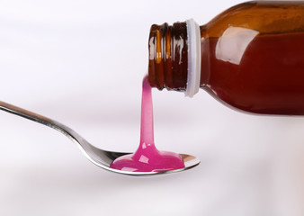 Pouring cough syrup into spoon on white background, closeup