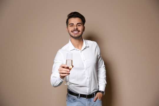 Handsome man with glass of champagne on color background