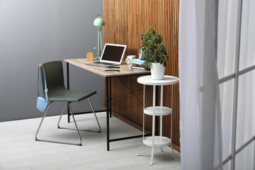 Stylish workplace interior with laptop on table near wooden wall. Space for text
