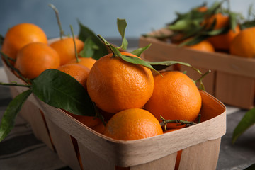 Fresh ripe tangerines with green leaves in crate on table