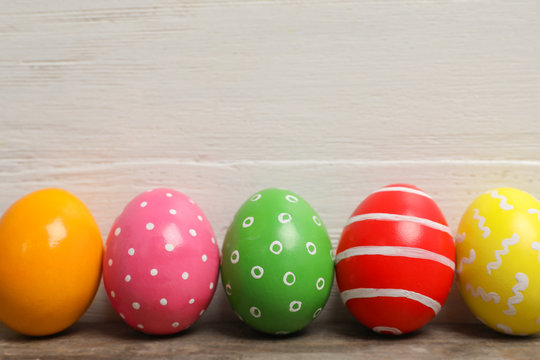 Decorated Easter eggs on table near wooden wall. Space for text