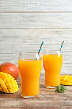 Fresh tropical mango juice and fruits on wooden table. Space for text