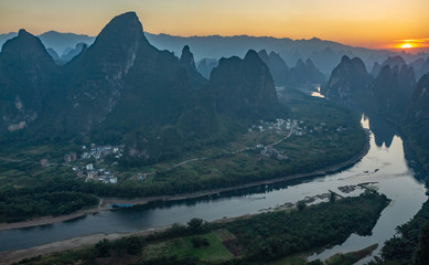 Sunrise over the Li River as seen from Xianggong mountain, Yangshuo, Guilin, China. Landscape is in silhouette with orange sun rising on upper right.