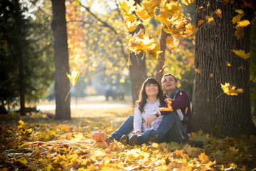 Loving couple sit on the leaves under a tree in the autumn park