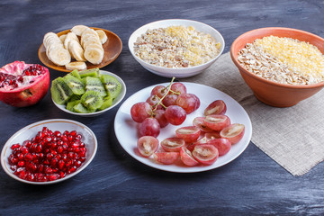 A set of plates with muesli, grapes, kiwi, pomegranate, banana on a black background.