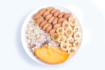 A plate with muesli, almonds, banana, persimmon isolated on white background.