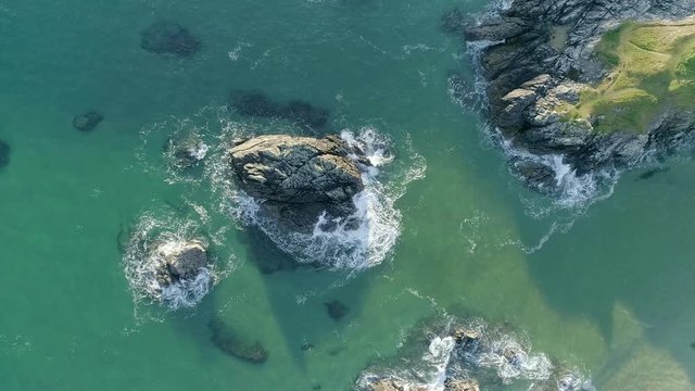 Zooming in from above on a large rock standing tall in the blue ocean water as the tide breaks below on Scotland's north coast in the Sango Sands area of Durness