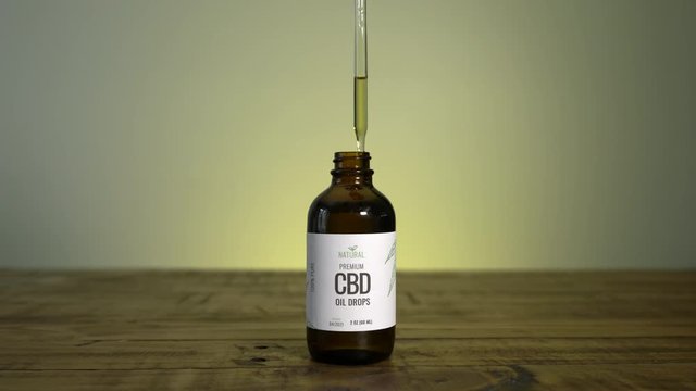 Person takes dropper out of bottle of CBD oil and drops some oil back into the bottle.