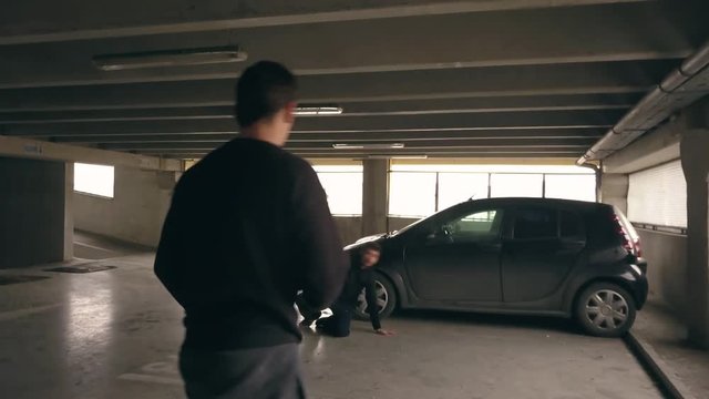 Man attacked in a parking deck defends himself and fights back. Two men fighting near a parked car in a garage. Actors perform a choreographed fighting stunt scene for a movie.