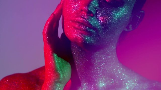 Fashion model woman in colorful bright sparkles and neon lights posing in studio, portrait of beautiful sexy girl. Art design colorful vivid makeup. Slow motion 4K UHD video footage. 3840X2160
