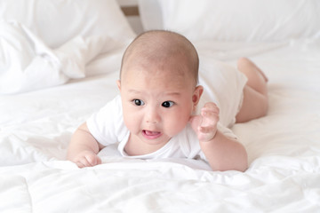 Beautiful smiling baby crawling for the first time. Adorable baby boy in white sunny bedroom. Newborn child relaxing on bed. Nursery for young children concept. - Image