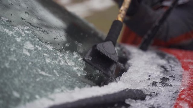 Man cleaning and scraping ice from car windshield in snow slowmo