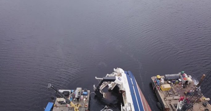 Backwards flying aerial drone shot of a capsized overturned ship being repaired by rescue boats on the ocean in the aftermath of Hurricane Michael