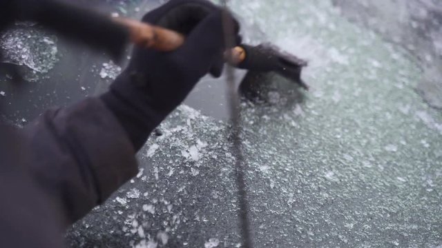 Man cleaning and scraping ice from car windshield in snow slowmo