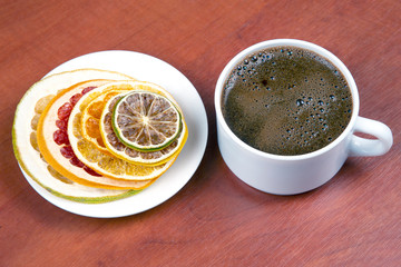 Dried slices of various citrus fruits and black coffee in a white Cup
