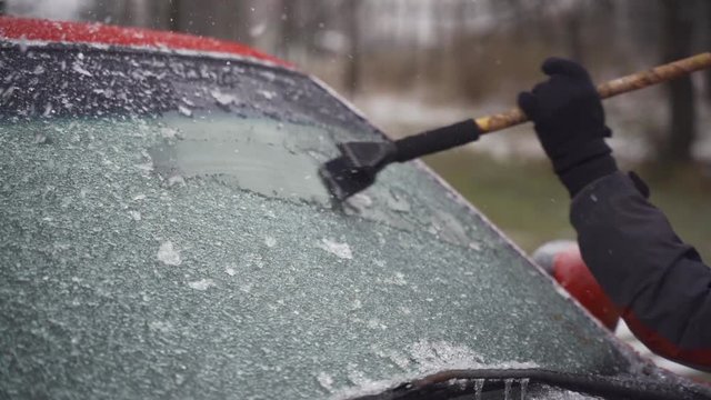 Man cleaning and scraping ice from car windshield in snow