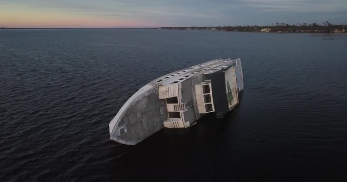 Rotating aerial shot of an overturned capsized passenger ship with a happy holidays sign off the coast of Panama City with a sunset ocean horizon
