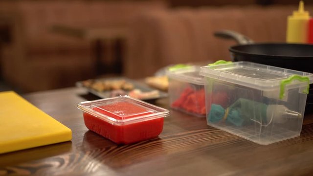 Different products packed in transperent lunchboxes in kitchen of a cafe lying on a wood table. There are a frying pan, ketchup, mustard. Close up concept. The camera slowly moving from left to right