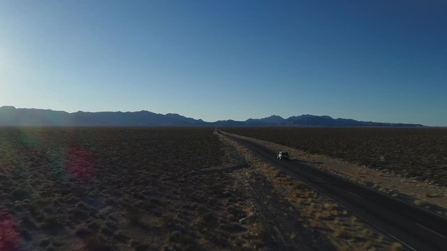 A tracking shot of a car moving in along an isolated road in a desert towards imposing mountains