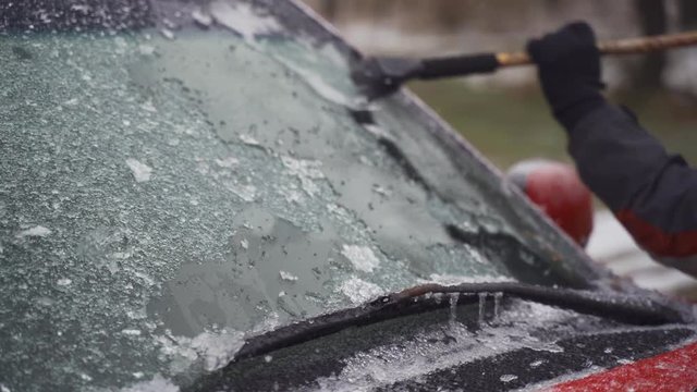 Man cleaning and scraping ice from car windshield in snow slowmo