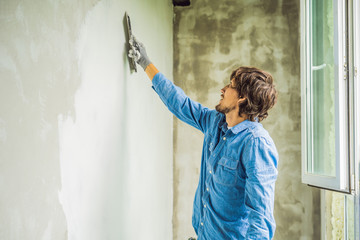 master is applying white putty on a wall and smearing by putty knife in a room of renovating house...
