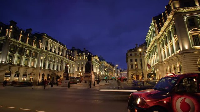 Night time time-lapse of zooming London traffic and people filmed on the corner of Regent St. and Pall Mall with grand buildings illuminated in the background.