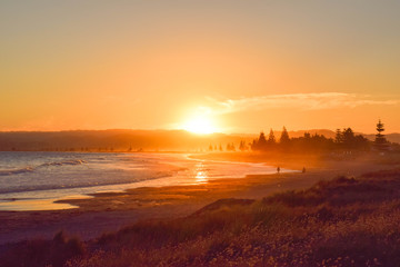 Couple walk along the empty beach at sunset in Gisborne, New Zealand.