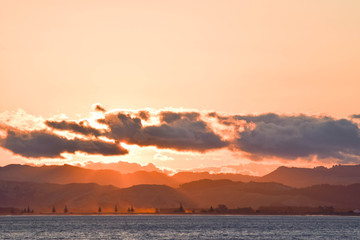 The darkening clouds hide a bright sunset above the dark hills in Gisborne, New Zealand.
