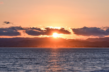 A circuar orange sunset shaped by surrounding clouds at the beach in Gisborne, New Zealand.