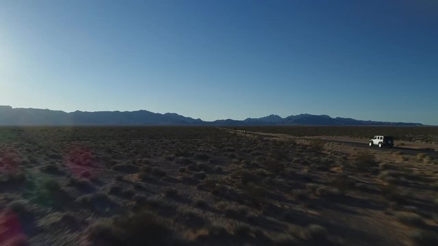 A tracking shot of a car driving in the middle of an isolated road in the desert towards the mountains