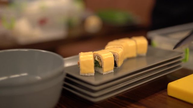 Male hand in blue rubber glove putting sushi rolls on the grey sushi plate set in the cafe kitchen. Preparing sushi set for the client. Blurred background