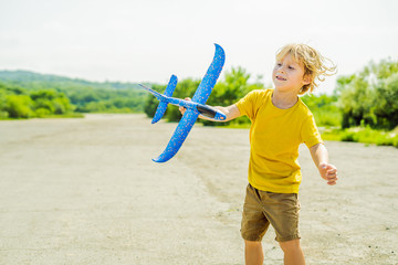 Happy kid playing with toy airplane against old runway background. Traveling with kids concept
