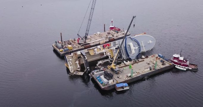 Aerial drone shot panning across a sideways capsized ship on the ocean with rescue boats and platforms in the aftermath of Hurricane Michael