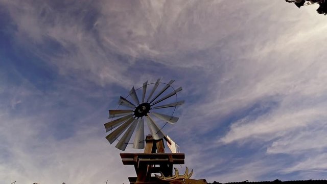 cowboy style, old farm or prairie  wind pump spinning against a blue sunny sky