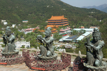 Color, daytime landscape photo of the Po Lin Monastery on Lantau Island, Hong Kong, China. Buddhist bodhisattva statue in foreground, hills in background.