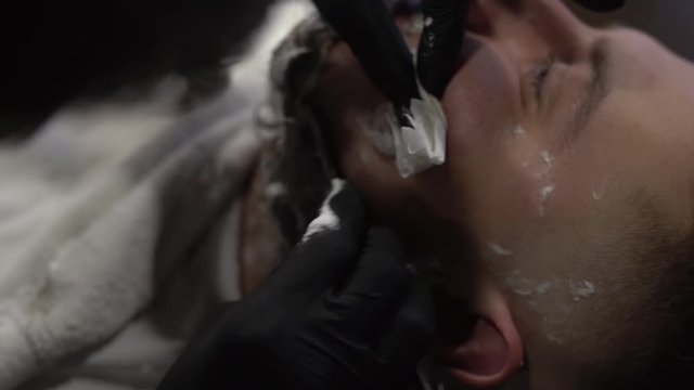 Tattoed hand of a barberman cleaning shaving blades by spraying them with special liquid to make them shiny and clean. Close-up concept