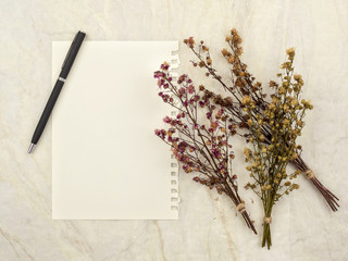 Top view of note pad paper with pen and group of bouquet dried and wilted multiple color Gypsophila flowers on matt marble background for text, letter, message or verse