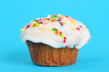 Delicious homemade muffin with white fondant icing and colorful sugar sprinkles on a bright turquoise blue background. Close up of a festive cupcake in vibrant colors