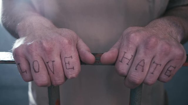 Extreme close-up of prison bars as a prisoner walks up to the bars and holds on to them. We see that he has "love" and "hate" tattooed on his fingers and then leaves after a beat.