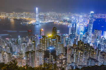 Hong Kong skyline at night as seen from Victoria Peak. Illuminated skyscrapers in foreground, Hong Kong harbor in background.