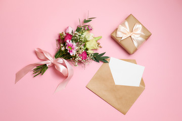 Valentines day composition: bouquet of flowers, gift box with ribbon bow, kraft envelope with greeting card lay at pink background. Woman's day card template, flat layout, top view, overhead.