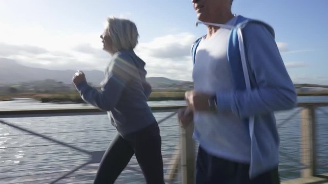 Fit healthy senior couple jogging along river together