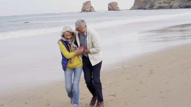 Full length of attractive senior couple walking and smiling on beach in fall 